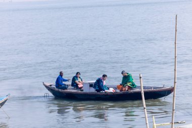 Varanasi, Uttar Pradesh, Hindistan - Kasım 2022: Turistler sabah erken saatlerde Varanasi 'deki martı sürüsüyle birlikte nehir çetelerinde tekne gezintisi yapıyorlar. Tahta teknede yelken açan kayıkçı.