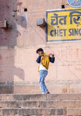 Varanasi, Uttar Pradesh, Hindistan - Kasım 2022: Varanasi 'deki nehir çetelerinin yakınlarındaki ghat üzerinde dans eden genç bir çocuğun portresi. Varanasi 'deki Ghat' ler birçok sanat çalışması ve gösterisine tanıklık ediyor..