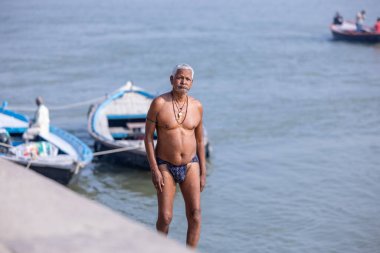 Varanasi, Uttar Pradesh, Hindistan - Kasım 2022: Varanasi şehrindeki nehir çetelerinin yakınlarındaki ghat merdivenlerinde yürüyen kimliği belirsiz Hintli yaşlı erkek portresi.