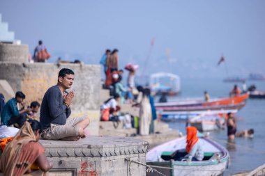 Varanasi, Uttar Pradesh, Hindistan - Kasım 2022: Gündoğumunda nehir çeteleri yakınlarında meditasyon ve yoga yapan genç bir erkek rahibin portresi.