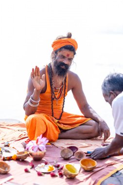 Varanasi, Uttar Pradesh, Hindistan - Kasım 2022: Varanasi şehrinde geleneksel elbise içinde nehir çetelerinin yanındaki Assi ghat 'ta oturan kimliği belirsiz Hintli sadhu baba portresi.