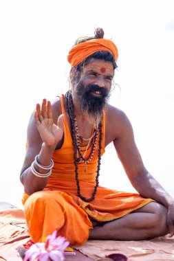 Varanasi, Uttar Pradesh, Hindistan - Kasım 2022: Varanasi şehrinde geleneksel elbise içinde nehir çetelerinin yanındaki Assi ghat 'ta oturan kimliği belirsiz Hintli sadhu baba portresi.