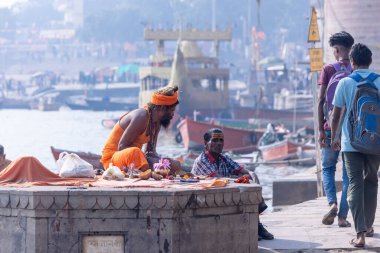 Varanasi, Uttar Pradesh, Hindistan - Kasım 2022: Varanasi şehrinde geleneksel elbise içinde nehir çetelerinin yanındaki Assi ghat 'ta oturan kimliği belirsiz Hintli sadhu baba portresi.