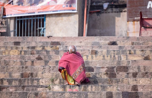 Varanasi, Uttar Pradesh, Hindistan - Kasım 2022: Varanasi şehrinde nehir çetelerinin yanındaki ghat merdivenlerinde oturan kimliği belirsiz Hintli yaşlı erkek portresi.