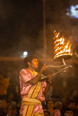 Varanasi, Uttar Pradesh, Hindistan - Kasım 2022: Ganga aarti, genç bir rahibin portresi, Assi Ghat 'ta akşam üzeri ateş ve ayinlerle geleneksel elbise giymiş nehir çetelerini icra ediyor..