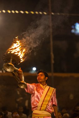 Varanasi, Uttar Pradesh, Hindistan - Kasım 2022: Ganga aarti, genç bir rahibin portresi, Assi Ghat 'ta akşam üzeri ateş ve ayinlerle geleneksel elbise giymiş nehir çetelerini icra ediyor..