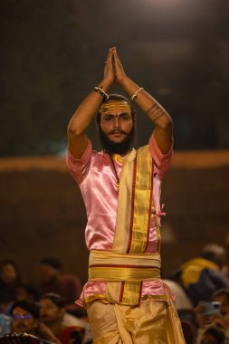 Varanasi, Uttar Pradesh, Hindistan - Kasım 2022: Ganga aarti, genç bir rahibin portresi, Assi Ghat 'ta akşam üzeri ateş ve ayinlerle geleneksel elbise giymiş nehir çetelerini icra ediyor..