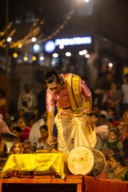 Varanasi, Uttar Pradesh, Hindistan - Kasım 2022: Ganga aarti, genç bir rahibin portresi, Assi Ghat 'ta akşam üzeri ateş ve ayinlerle geleneksel elbise giymiş nehir çetelerini icra ediyor..