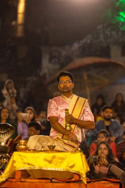 Varanasi, Uttar Pradesh, Hindistan - Kasım 2022: Ganga aarti, genç bir rahibin portresi, Assi Ghat 'ta akşam üzeri ateş ve ayinlerle geleneksel elbise giymiş nehir çetelerini icra ediyor..