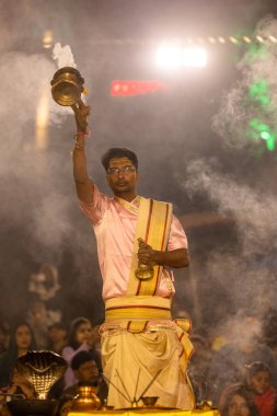 Varanasi, Uttar Pradesh, Hindistan - Kasım 2022: Ganga aarti, genç bir rahibin portresi, Assi Ghat 'ta akşam üzeri ateş ve ayinlerle geleneksel elbise giymiş nehir çetelerini icra ediyor..