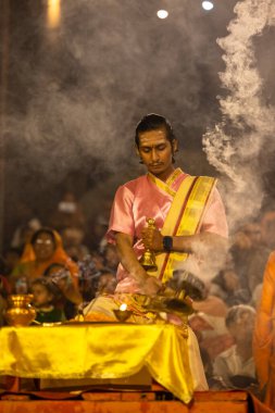 Varanasi, Uttar Pradesh, Hindistan - Kasım 2022: Ganga aarti, genç bir rahibin portresi, Assi Ghat 'ta akşam üzeri ateş ve ayinlerle geleneksel elbise giymiş nehir çetelerini icra ediyor..