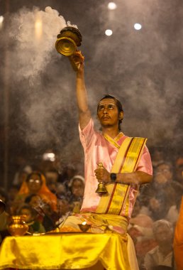 Varanasi, Uttar Pradesh, Hindistan - Kasım 2022: Ganga aarti, genç bir rahibin portresi, Assi Ghat 'ta akşam üzeri ateş ve ayinlerle geleneksel elbise giymiş nehir çetelerini icra ediyor..