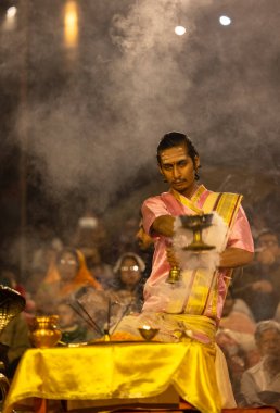 Varanasi, Uttar Pradesh, Hindistan - Kasım 2022: Ganga aarti, genç bir rahibin portresi, Assi Ghat 'ta akşam üzeri ateş ve ayinlerle geleneksel elbise giymiş nehir çetelerini icra ediyor..