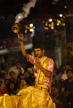 Varanasi, Uttar Pradesh, Hindistan - Kasım 2022: Ganga aarti, genç bir rahibin portresi, Assi Ghat 'ta akşam üzeri ateş ve ayinlerle geleneksel elbise giymiş nehir çetelerini icra ediyor..