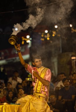 Varanasi, Uttar Pradesh, Hindistan - Kasım 2022: Ganga aarti, genç bir rahibin portresi, Assi Ghat 'ta akşam üzeri ateş ve ayinlerle geleneksel elbise giymiş nehir çetelerini icra ediyor..
