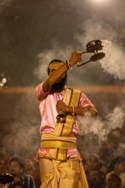 Varanasi, Uttar Pradesh, Hindistan - Kasım 2022: Ganga aarti, genç bir rahibin portresi, Assi Ghat 'ta akşam üzeri ateş ve ayinlerle geleneksel elbise giymiş nehir çetelerini icra ediyor..