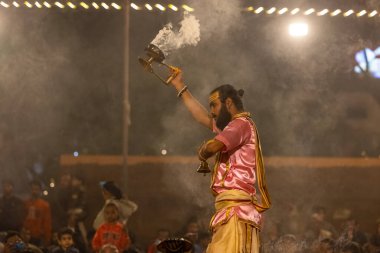 Varanasi, Uttar Pradesh, Hindistan - Kasım 2022: Ganga aarti, genç bir rahibin portresi, Assi Ghat 'ta akşam üzeri ateş ve ayinlerle geleneksel elbise giymiş nehir çetelerini icra ediyor..