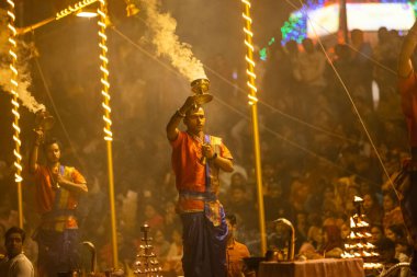 Varanasi, Uttar Pradesh, India - November 2022: Ganga aarti, Portrait of an young priest performing river ganges evening aarti at assi Ghat in traditional dress with fire flame and rituals. clipart