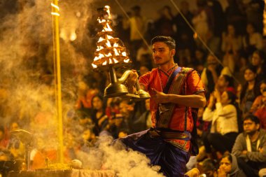Varanasi, Uttar Pradesh, Hindistan - Kasım 2022: Ganga aarti, genç bir rahibin portresi, Assi Ghat 'ta akşam üzeri ateş ve ayinlerle geleneksel elbise giymiş nehir çetelerini icra ediyor..