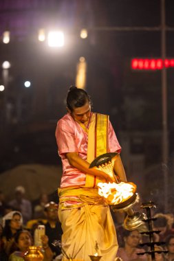 Varanasi, Uttar Pradesh, Hindistan - Kasım 2022: Ganga aarti, genç bir rahibin portresi, Assi Ghat 'ta akşam üzeri ateş ve ayinlerle geleneksel elbise giymiş nehir çetelerini icra ediyor..