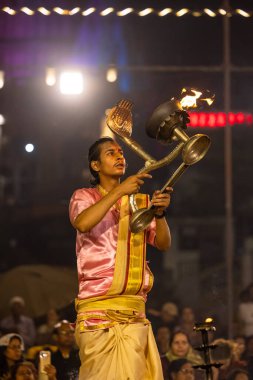 Varanasi, Uttar Pradesh, Hindistan - Kasım 2022: Ganga aarti, genç bir rahibin portresi, Assi Ghat 'ta akşam üzeri ateş ve ayinlerle geleneksel elbise giymiş nehir çetelerini icra ediyor..