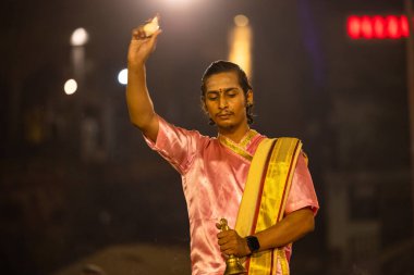 Varanasi, Uttar Pradesh, Hindistan - Kasım 2022: Ganga aarti, genç bir rahibin portresi, Assi Ghat 'ta akşam üzeri ateş ve ayinlerle geleneksel elbise giymiş nehir çetelerini icra ediyor..