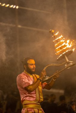 Varanasi, Uttar Pradesh, Hindistan - Kasım 2022: Ganga aarti, genç bir rahibin portresi, Assi Ghat 'ta akşam üzeri ateş ve ayinlerle geleneksel elbise giymiş nehir çetelerini icra ediyor..