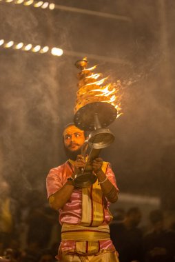 Varanasi, Uttar Pradesh, Hindistan - Kasım 2022: Ganga aarti, genç bir rahibin portresi, Assi Ghat 'ta akşam üzeri ateş ve ayinlerle geleneksel elbise giymiş nehir çetelerini icra ediyor..