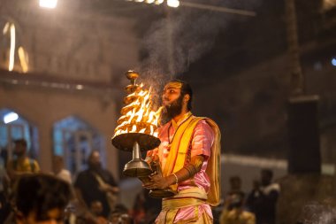 Varanasi, Uttar Pradesh, Hindistan - Kasım 2022: Ganga aarti, genç bir rahibin portresi, Assi Ghat 'ta akşam üzeri ateş ve ayinlerle geleneksel elbise giymiş nehir çetelerini icra ediyor..