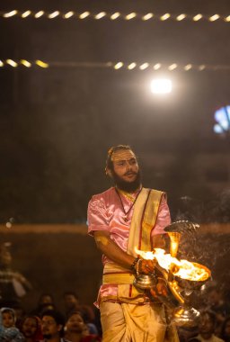 Varanasi, Uttar Pradesh, Hindistan - Kasım 2022: Ganga aarti, genç bir rahibin portresi, Assi Ghat 'ta akşam üzeri ateş ve ayinlerle geleneksel elbise giymiş nehir çetelerini icra ediyor..