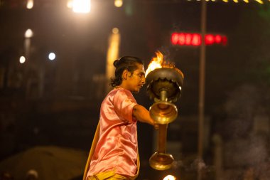 Varanasi, Uttar Pradesh, Hindistan - Kasım 2022: Ganga aarti, genç bir rahibin portresi, Assi Ghat 'ta akşam üzeri ateş ve ayinlerle geleneksel elbise giymiş nehir çetelerini icra ediyor..