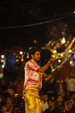Varanasi, Uttar Pradesh, Hindistan - Kasım 2022: Ganga aarti, genç bir rahibin portresi, Assi Ghat 'ta akşam üzeri ateş ve ayinlerle geleneksel elbise giymiş nehir çetelerini icra ediyor..