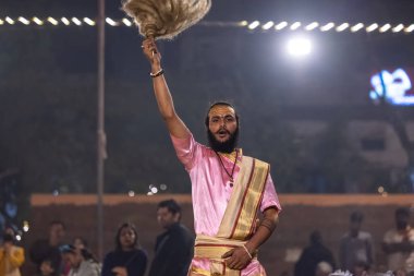 Varanasi, Uttar Pradesh, Hindistan - Kasım 2022: Ganga aarti, genç bir rahibin portresi, Assi Ghat 'ta akşam üzeri ateş ve ayinlerle geleneksel elbise giymiş nehir çetelerini icra ediyor..