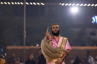 Varanasi, Uttar Pradesh, Hindistan - Kasım 2022: Ganga aarti, genç bir rahibin portresi, Assi Ghat 'ta akşam üzeri ateş ve ayinlerle geleneksel elbise giymiş nehir çetelerini icra ediyor..