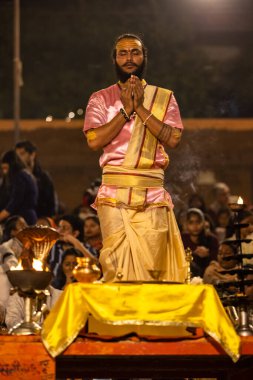 Varanasi, Uttar Pradesh, Hindistan - Kasım 2022: Ganga aarti, genç bir rahibin portresi, Assi Ghat 'ta akşam üzeri ateş ve ayinlerle geleneksel elbise giymiş nehir çetelerini icra ediyor..