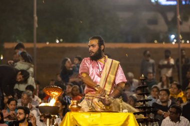 Varanasi, Uttar Pradesh, Hindistan - Kasım 2022: Ganga aarti, genç bir rahibin portresi, Assi Ghat 'ta akşam üzeri ateş ve ayinlerle geleneksel elbise giymiş nehir çetelerini icra ediyor..