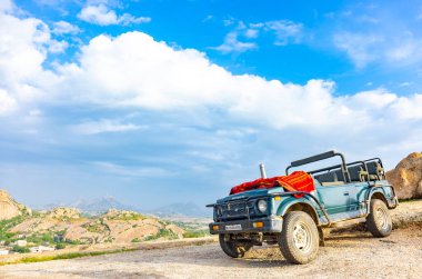 Jawai, Rajasthan, Hindistan - Eylül 2021: Hindistan 'ın Rajasthan kentindeki Aravalli dağlarının manzarası. Mavi gökyüzünün altındaki tepelerin tepesine bir safari cipi iniyor..