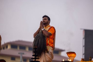 Varanasi, Uttar Pradesh, Hindistan - Kasım 2022: Ganga aarti, genç bir rahibin portresi, Assi Ghat 'ta akşam üzeri ateş ve ayinlerle geleneksel elbise giymiş nehir çetelerini icra ediyor..