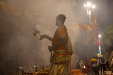 Varanasi, Uttar Pradesh, Hindistan - Kasım 2022: Ganga aarti, genç bir rahibin portresi, Assi Ghat 'ta akşam üzeri ateş ve ayinlerle geleneksel elbise giymiş nehir çetelerini icra ediyor..