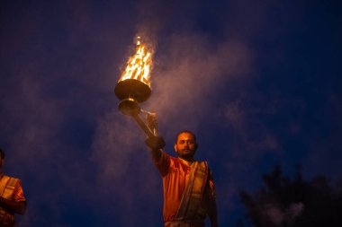 Varanasi, Uttar Pradesh, Hindistan - Kasım 2022: Ganga aarti, genç bir rahibin portresi, Assi Ghat 'ta akşam üzeri ateş ve ayinlerle geleneksel elbise giymiş nehir çetelerini icra ediyor..