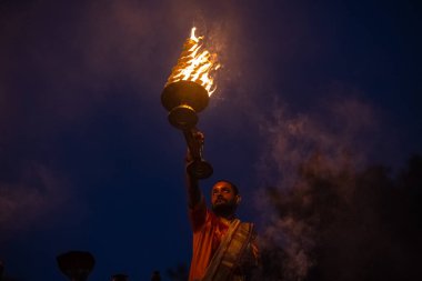 Varanasi, Uttar Pradesh, Hindistan - Kasım 2022: Ganga aarti, genç bir rahibin portresi, Assi Ghat 'ta akşam üzeri ateş ve ayinlerle geleneksel elbise giymiş nehir çetelerini icra ediyor..