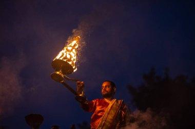 Varanasi, Uttar Pradesh, Hindistan - Kasım 2022: Ganga aarti, genç bir rahibin portresi, Assi Ghat 'ta akşam üzeri ateş ve ayinlerle geleneksel elbise giymiş nehir çetelerini icra ediyor..