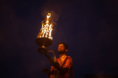 Varanasi, Uttar Pradesh, Hindistan - Kasım 2022: Ganga aarti, genç bir rahibin portresi, Assi Ghat 'ta akşam üzeri ateş ve ayinlerle geleneksel elbise giymiş nehir çetelerini icra ediyor..