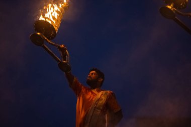 Varanasi, Uttar Pradesh, Hindistan - Kasım 2022: Ganga aarti, genç bir rahibin portresi, Assi Ghat 'ta akşam üzeri ateş ve ayinlerle geleneksel elbise giymiş nehir çetelerini icra ediyor..