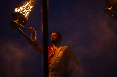 Varanasi, Uttar Pradesh, Hindistan - Kasım 2022: Ganga aarti, genç bir rahibin portresi, Assi Ghat 'ta akşam üzeri ateş ve ayinlerle geleneksel elbise giymiş nehir çetelerini icra ediyor..