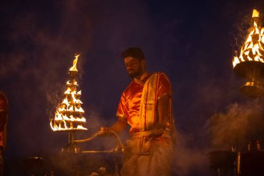 Varanasi, Uttar Pradesh, Hindistan - Kasım 2022: Ganga aarti, genç bir rahibin portresi, Assi Ghat 'ta akşam üzeri ateş ve ayinlerle geleneksel elbise giymiş nehir çetelerini icra ediyor..