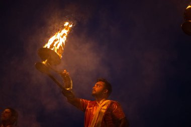 Varanasi, Uttar Pradesh, Hindistan - Kasım 2022: Ganga aarti, genç bir rahibin portresi, Assi Ghat 'ta akşam üzeri ateş ve ayinlerle geleneksel elbise giymiş nehir çetelerini icra ediyor..