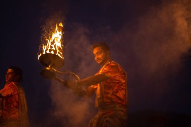 Varanasi, Uttar Pradesh, Hindistan - Kasım 2022: Ganga aarti, genç bir rahibin portresi, Assi Ghat 'ta akşam üzeri ateş ve ayinlerle geleneksel elbise giymiş nehir çetelerini icra ediyor..