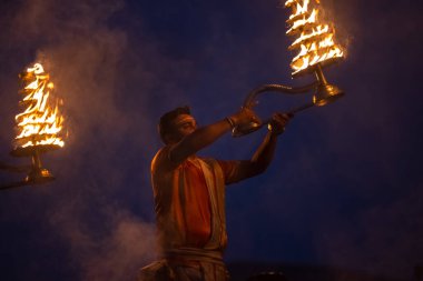 Varanasi, Uttar Pradesh, Hindistan - Kasım 2022: Ganga aarti, genç bir rahibin portresi, Assi Ghat 'ta akşam üzeri ateş ve ayinlerle geleneksel elbise giymiş nehir çetelerini icra ediyor..
