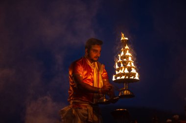 Varanasi, Uttar Pradesh, Hindistan - Kasım 2022: Ganga aarti, genç bir rahibin portresi, Assi Ghat 'ta akşam üzeri ateş ve ayinlerle geleneksel elbise giymiş nehir çetelerini icra ediyor..